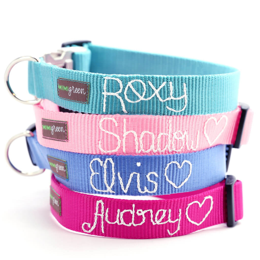 A stack of four hand embroidered dog collars with the names Roxy, Shadow, Elvis, and Audrey personalized on each